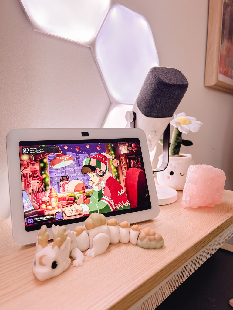 An Amazon Echo Show sits on the cosy gaming desk setup infront of a microphone and Nanoleaf hexagon lights in the background. 